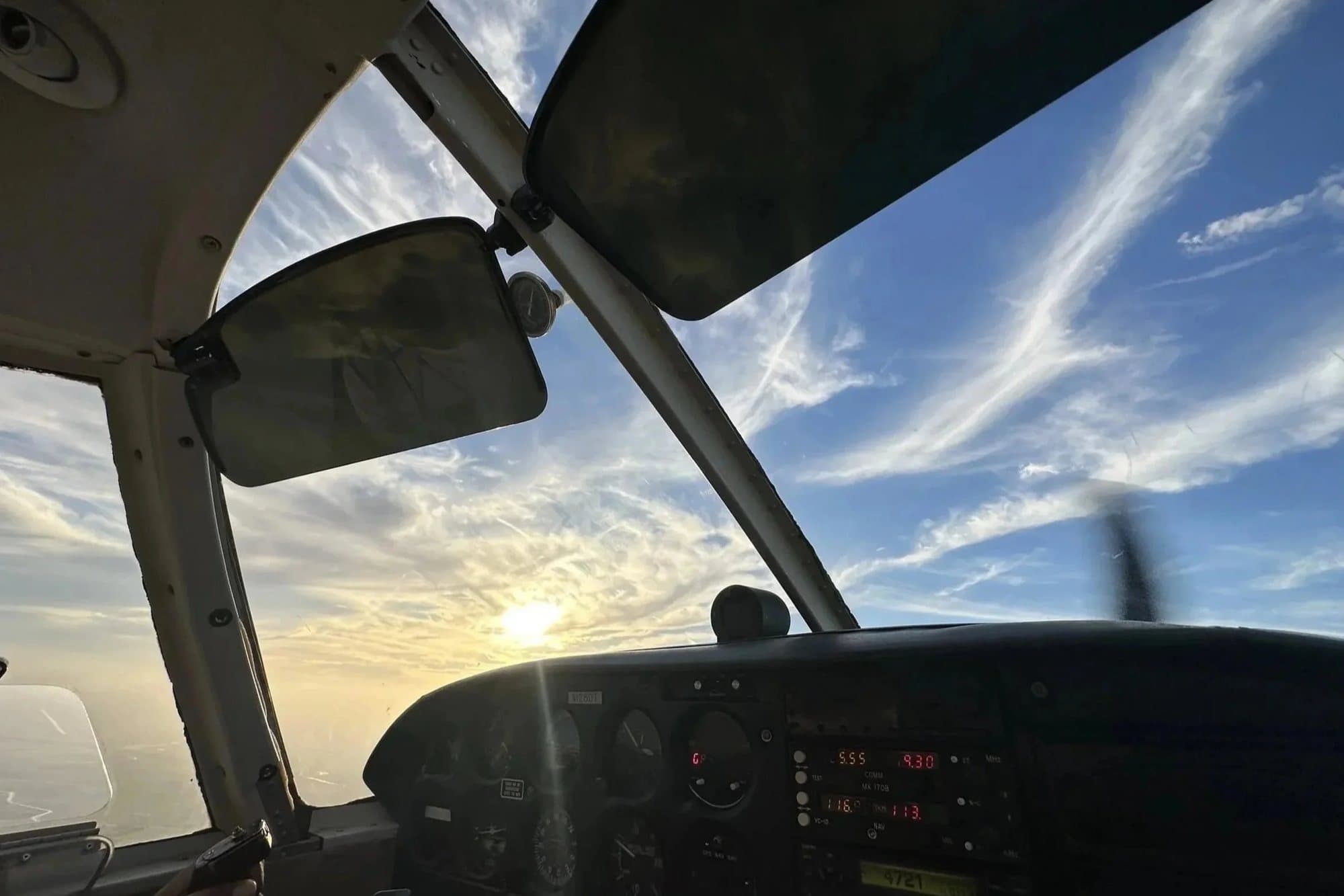 View through the windshield of a training aircraft toward a bright sky streaked with clouds