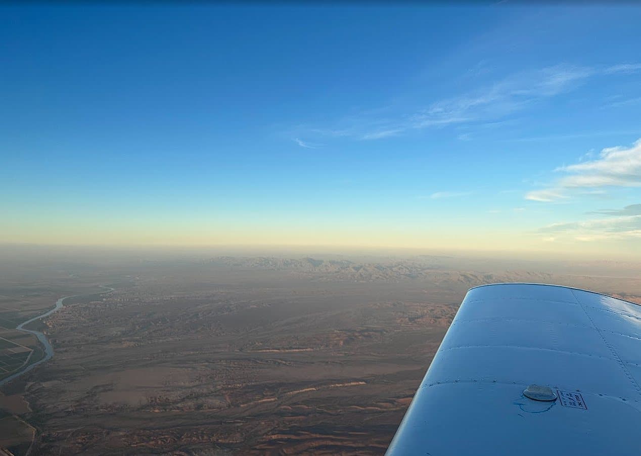 A training aircraft's wing above the desert under a clear blue sky